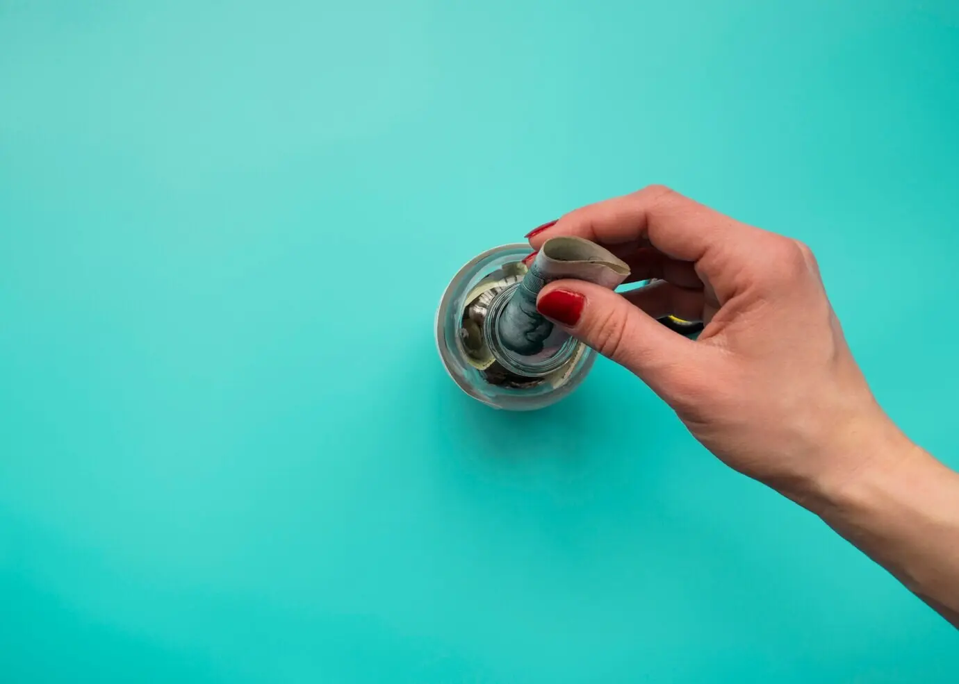 Eine Hand steckt Geld in ein Glas.